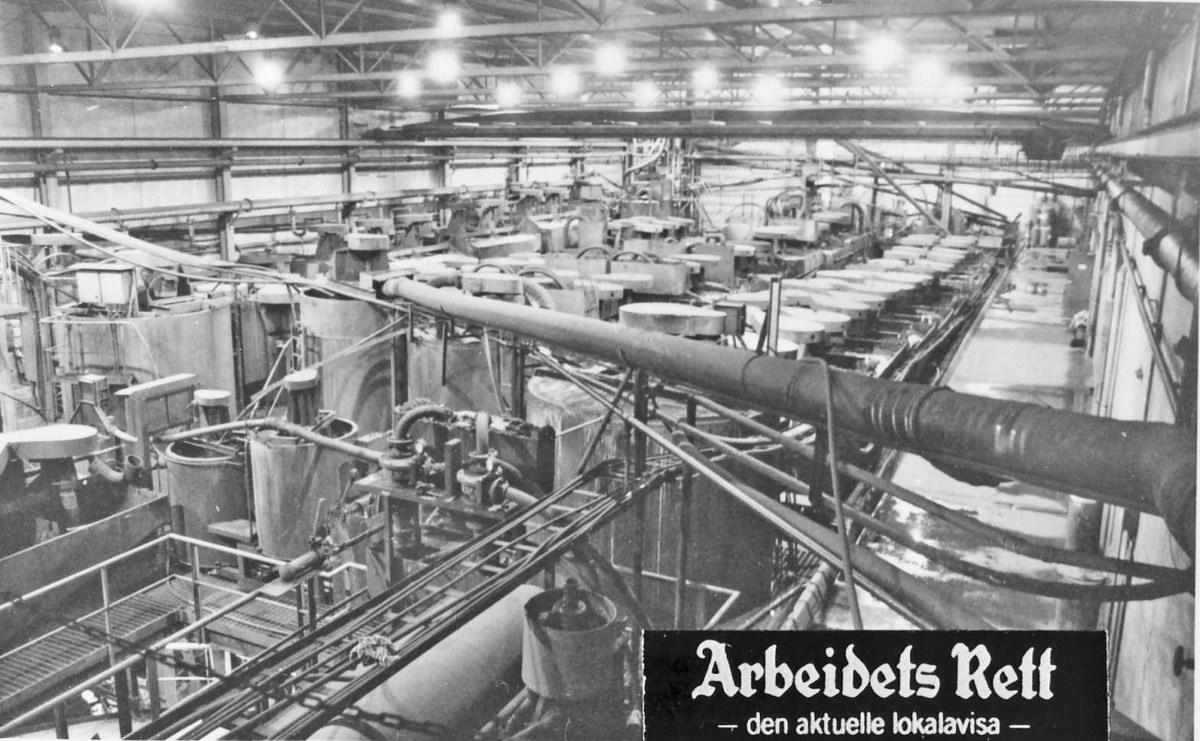 Black and white photo of an industrial factory interior with machinery, pipes, rods, and ceiling lights, featuring text at the bottom reading "Arbeibets Rett - den Aktuelle Lokalavisa".