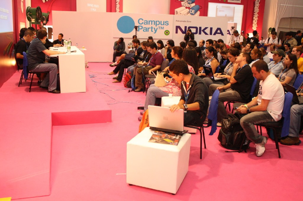 Conference with audience seated facing a stage where speakers engage with media and owners, featuring a large hoarding in the background.