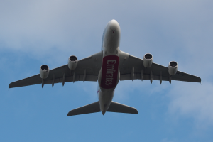 Ein Emirates Airbus A380-800-Flugzeug im Flug, mit ausgebreiteten Flügeln und aktiven Triebwerken, das durch einen Himmel mit weißen, flauschigen Wolken fliegt.
