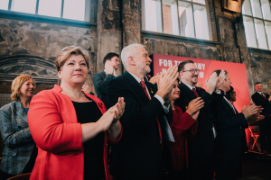 Menschen in einer Menge, die vor einem Gebäude mit einem Banner 'Wahlsieg.' jubeln