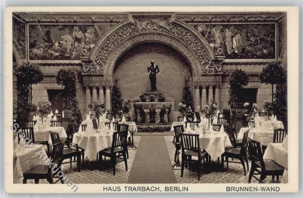 Schwarzes und weißes Foto eines alten Berliner Restaurantinnenraums mit Tischen, Stühlen, Blumenvasen, einer Statue im Hintergrund, Wandskulpturen, Pflanzen und Text unten.