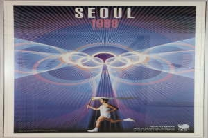 Eine Person, die mit den Olympischen Ringen im Hintergrund läuft und die Wörter "Olympische Spiele" über ein Plakat für die Olympischen Spiele 1988 in Seoul geschrieben sind.