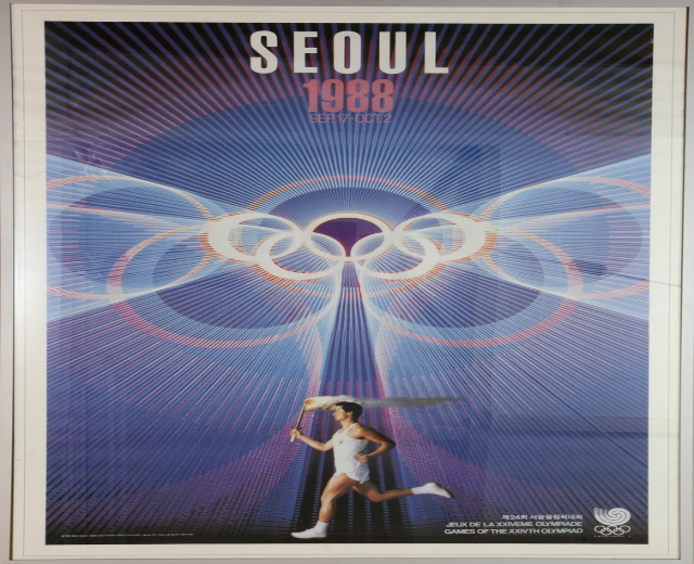 Eine Person, die mit den Olympischen Ringen im Hintergrund läuft und die Wörter "Olympische Spiele" über ein Plakat für die Olympischen Spiele 1988 in Seoul geschrieben sind.