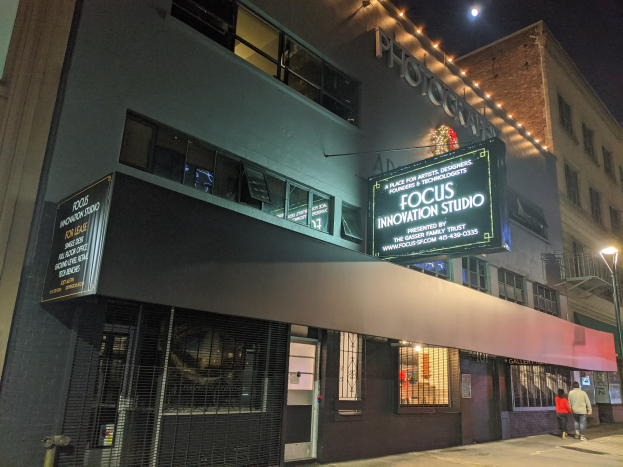 Außenansicht des Focus Innovation Studios in New York City bei Nacht, mit beleuchteten Gebäuden, Menschen auf dem Bürgersteig und sichtbarem Himmel.