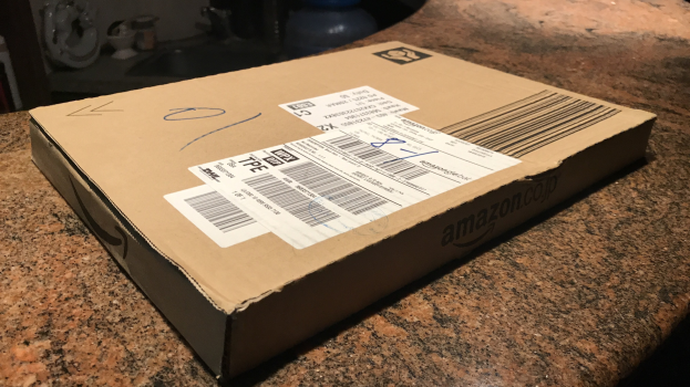Kartonbox mit der Aufschrift "Amazon Prime Day" unopened auf einer Arbeitsplatte mit einigen Gegenständen im Hintergrund.