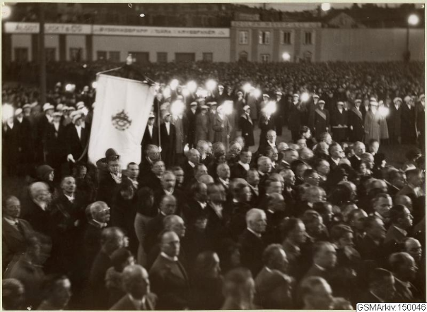 Schwarzes und weißes Foto einer großen Menge vor einem Gebäude, mit einer Person, die eine Fahne hält, Polen und Lichter im Hintergrund und dem Text "Gustav Klimts Rede an der Berliner Mauer" unten.