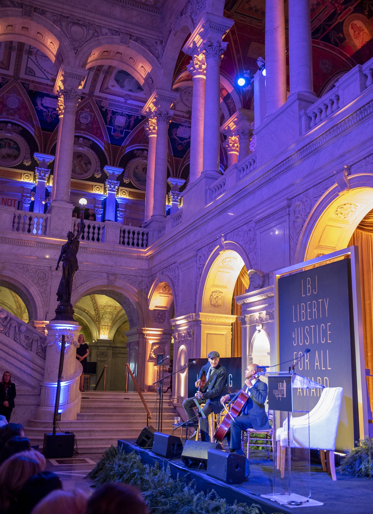 Group of people seated on a stage with musicians, a podium, and a board during the Liberty Justice for All Award Ceremony in New York City.