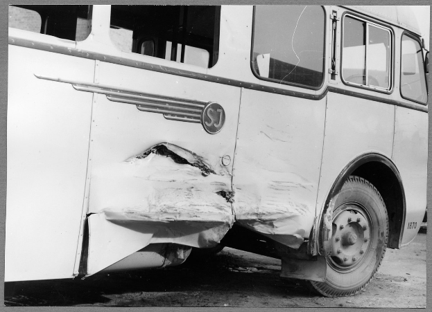 Schwarz-weißes Foto eines beschädigten Busses am Straßenrand mit einer eingedrückten Front, zersplitterten Fenstern und einer offenen Fahrertür, die das Innere zeigt.