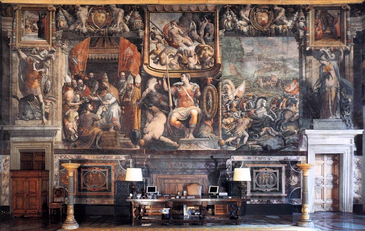 Großer Raum mit einem prominenten Gemälde an der Wand, einem Tisch mit Gegenständen, zwei Lampen, zwei Türen und einem Teppich, der sich im Palazzo della Signoria in Florenz, Italien, befindet.