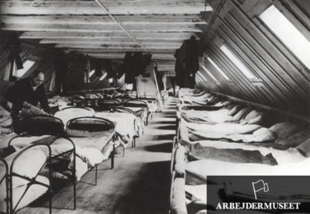 Ein Schwarz-Weiß-Foto eines Raumes voller Betten, mit einer Person auf der linken Seite und einem Text in der rechten unteren Ecke, der 'Arbejdermuseet in Berlin' lautet.