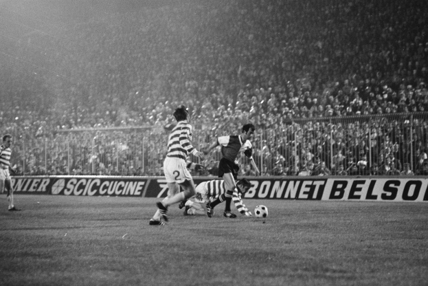 Schwarze-Weiß-Foto von Männern, die auf einem Feld Fußball spielen, mit Zuschauern auf den Tribünen und einem Banner mit der Aufschrift "Celtic v West Bromwich Albion - FA-Cup-Drittelfinale."