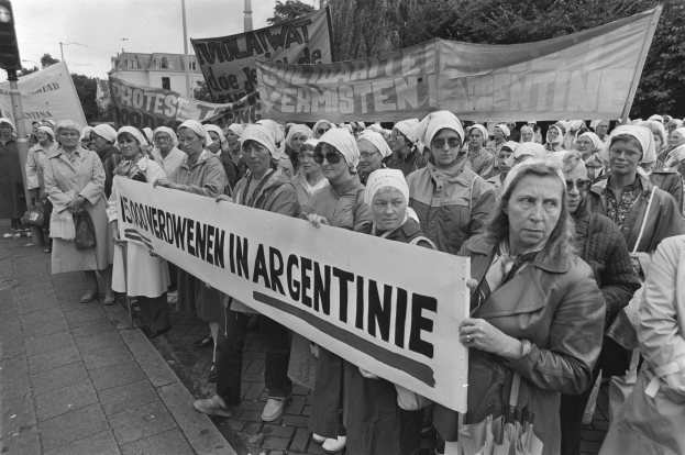 Eine Gruppe von Frauen hält ein Banner mit der Aufschrift "Argentinischer Frauenmarsch in Argentinien" vor Bäumen, Gebäuden, einer Ampel und einem bewölkten Himmel.