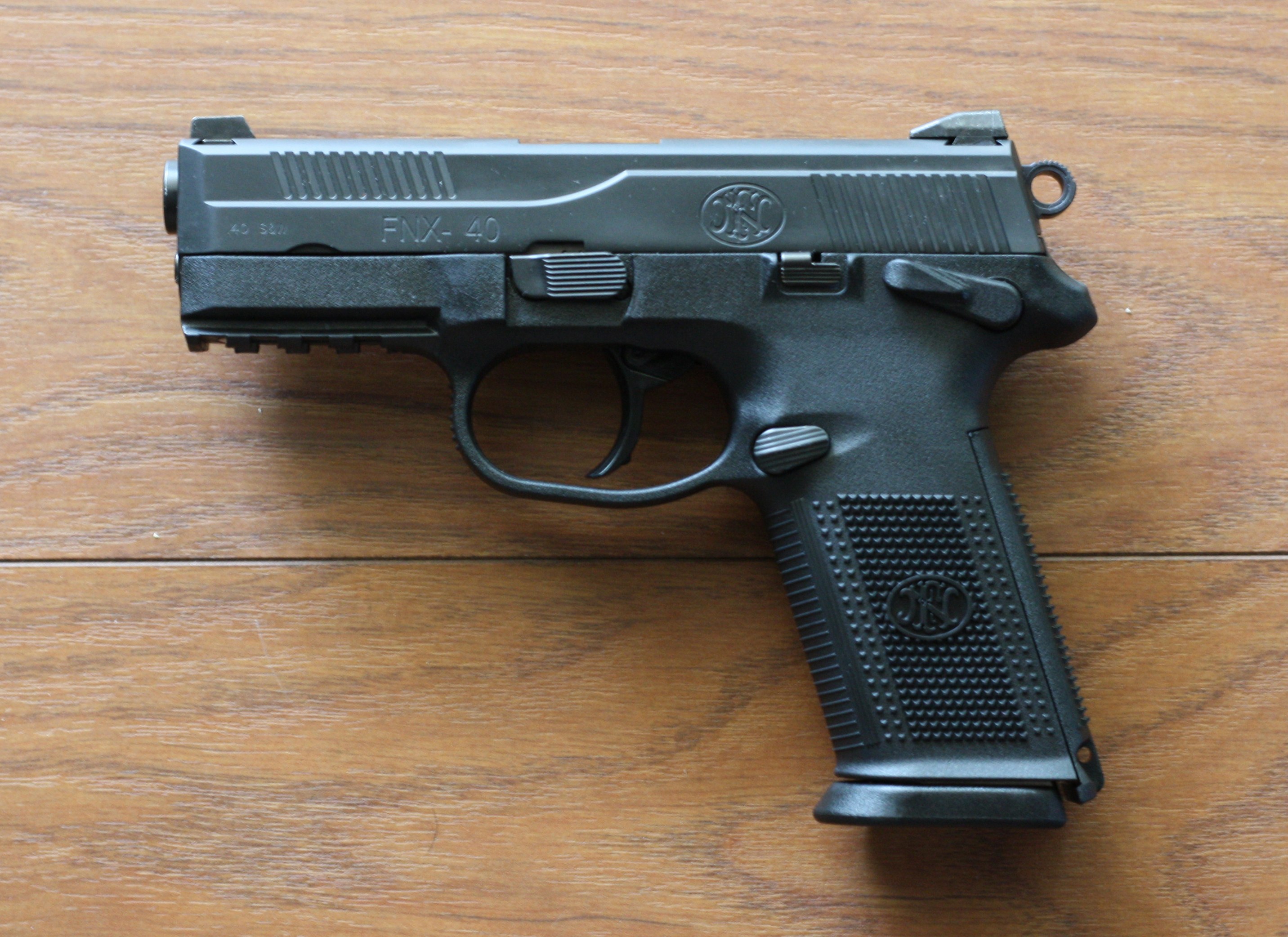 Eine schwarze Sig Sauer P320 X-Five 9mm Halbautomatikpistole mit einem strukturierten Griff und einem langen Lauf liegt auf einem hellen Holztisch.