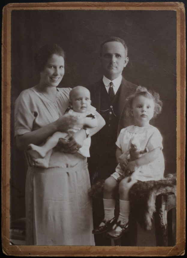 Ein Schwarz-Weiß-Foto von einem Mann und einer Frau, die nebeneinander stehen und jeweils ein Baby halten, mit einem dunklen Hintergrund.