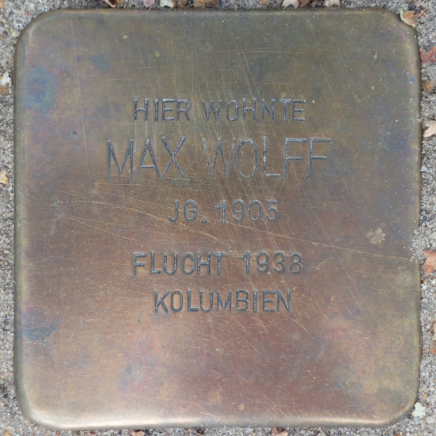 Metal plaque on the ground with the name "Max Wolff" inscribed, surrounded by dried leaves.