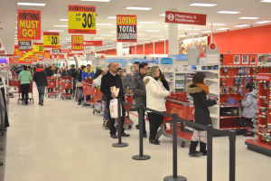 Ein volles Walmart-Geschäft mit Einkaufstaschen tragenden Kunden und Einkaufswagen, umgeben von Warenpräsentationsständern, Schildern und Deko, wahrscheinlich während eines Black Friday-Verkaufs.