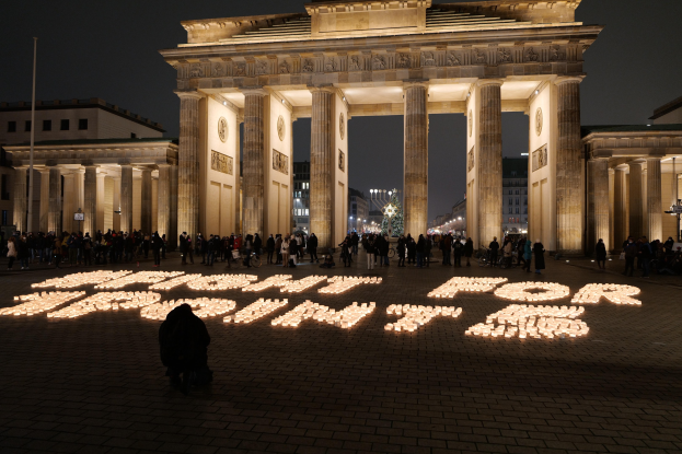 Eine Gruppe von Menschen steht vor dem beleuchteten Brandenburger Tor in Berlin, Deutschland, umgeben von Gebäuden, Pfählen und Lichtern; die Wörter "Kampf für die Freiheit" sind auf dem Boden zu sehen.