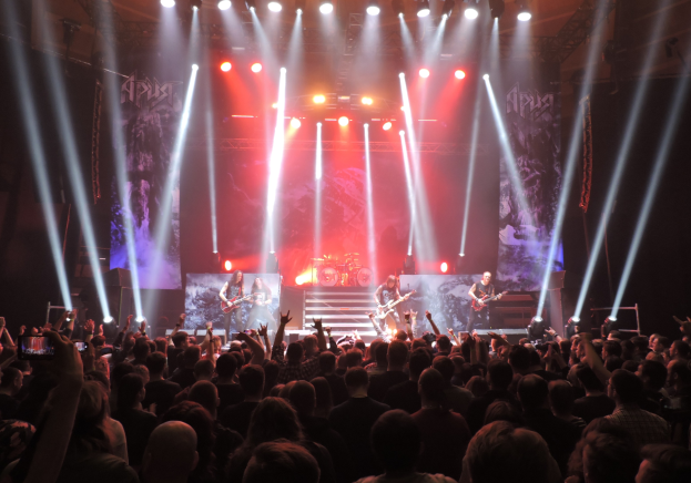 Eine Gruppe von Menschen, die auf einer hell erleuchteten Bühne spielt, einige mit Instrumenten, andere mit ihren Handys aufnehmen.