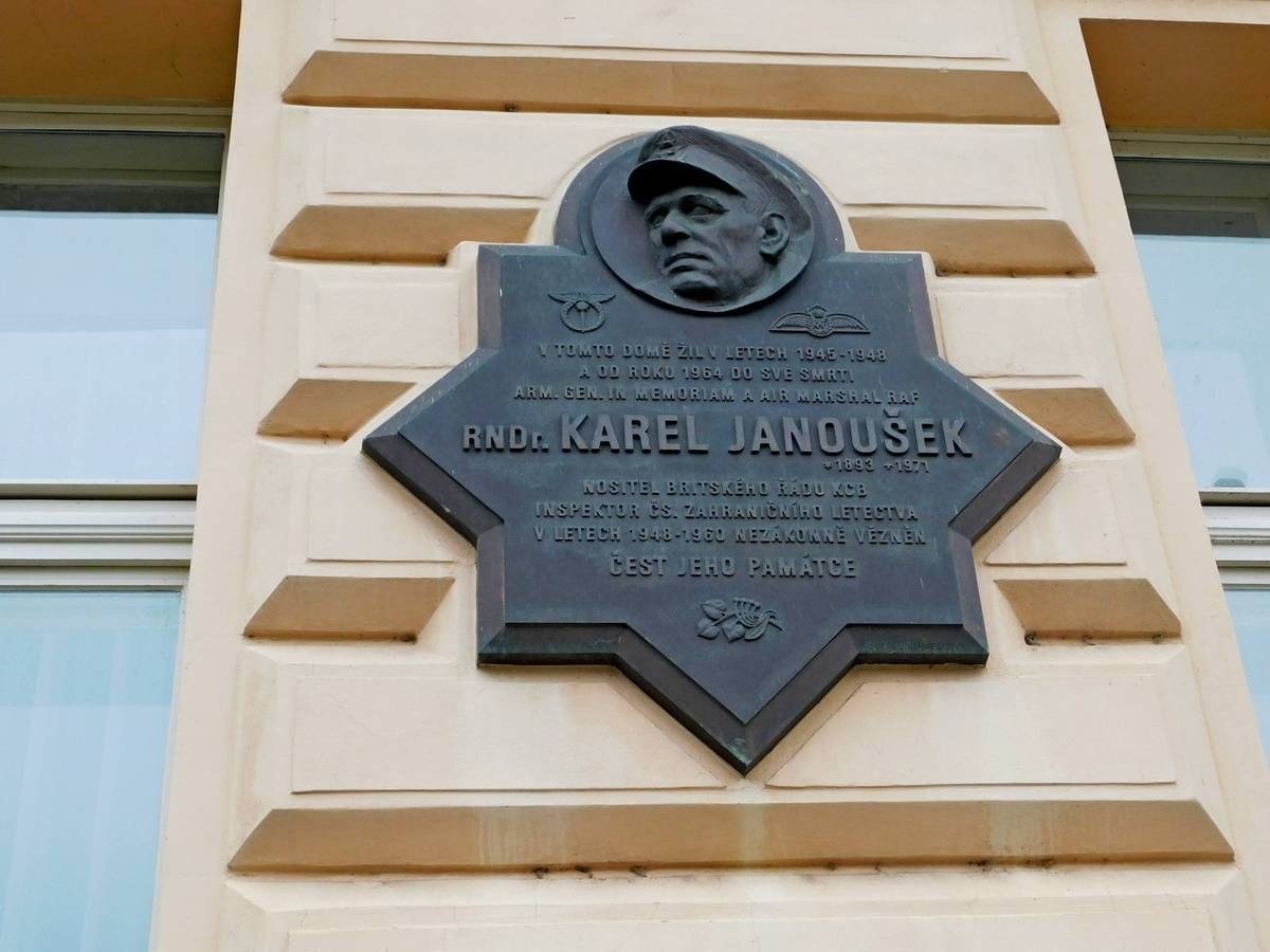 Plaque featuring an image of a man in a hat, mounted on a building with glass windows, inscribed with "Karel Janousek, the founder of the Soviet Union."