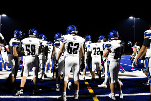 Eine Gruppe von Fußballspielern in Helmen und Stiefeln steht auf einem Feld, mit Flutlichtmasten im Hintergrund.
