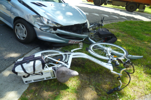 Auto auf der Seite der Straße mit einem Fahrrad in der Nähe auf dem Gras liegend, Bäume und ein klarer blauer Himmel im Hintergrund.