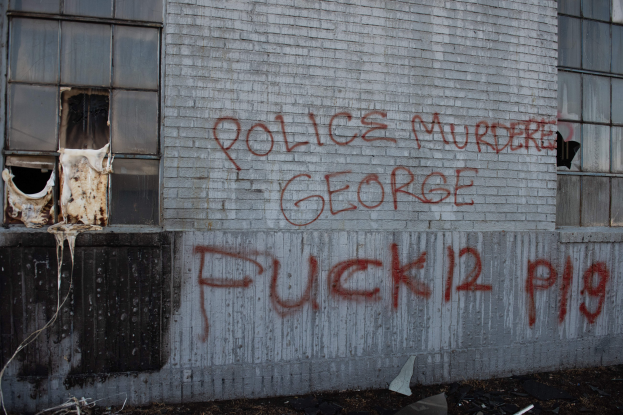 Ein Gebäude mit Graffiti, das "Polizei M"rdet George Fuck 12 P19" auf der Seite trägt, mit Fenstern und verschiedenen Gegenständen vorne drauf.