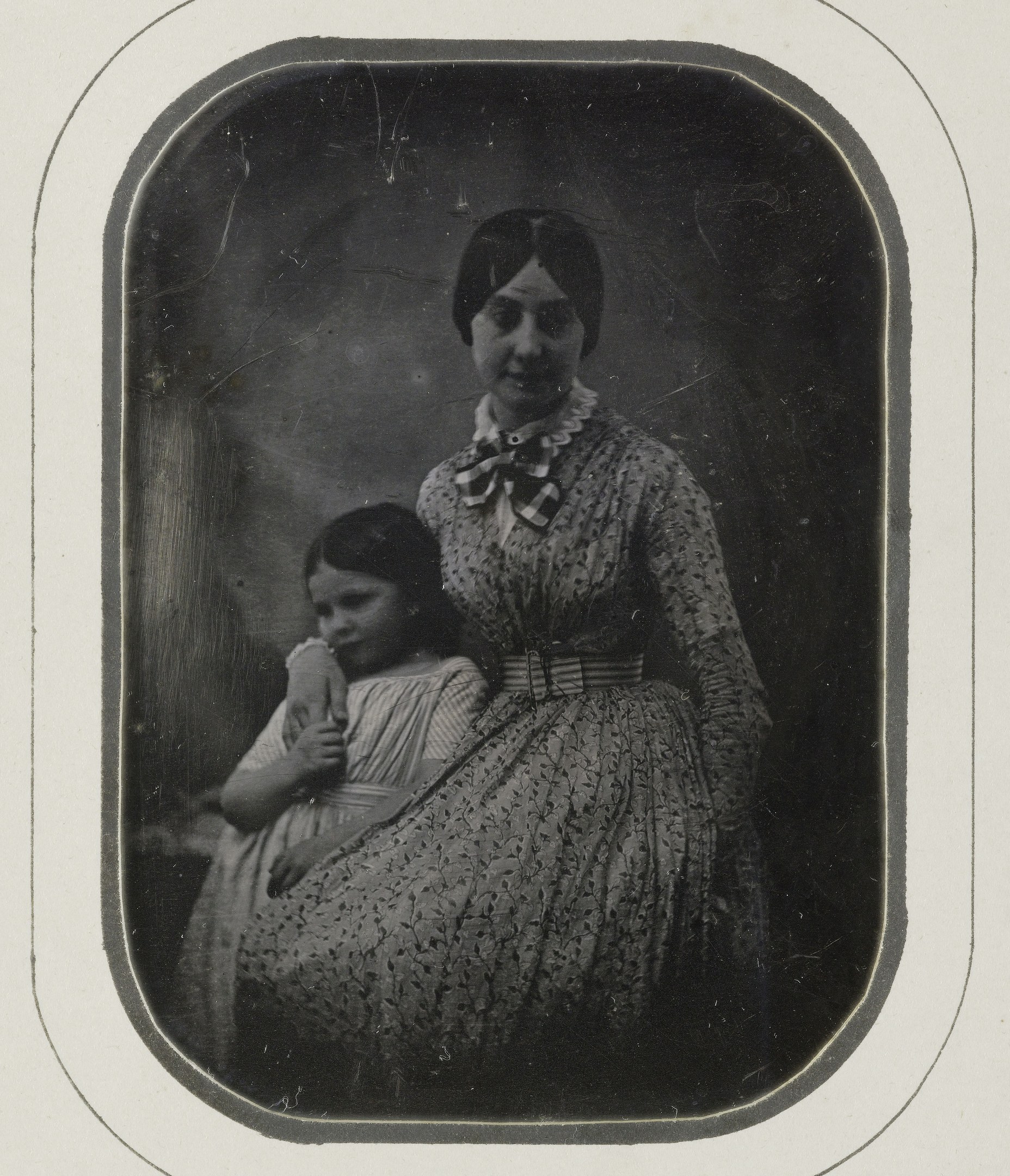 Black and white photo of a woman holding a child, with a gentle expression on her face and the child looking up with a contented smile.