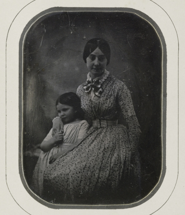 Black and white photo of a woman holding a child, with a gentle expression on her face and the child looking up with a contented smile.