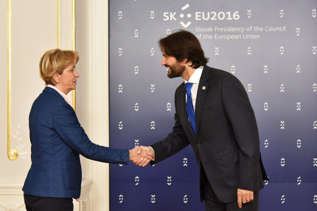Bundeskanzlerin Angela Merkel und Bundeskanzler Joachim Gauck schütteln sich lachend vor einer Wand mit einem 'EU-Gipfel'-Schild und einer Tür die Hände.
