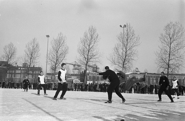 Schwarzes Bild von Menschen, die Eis-Hockey im Schnee spielen, mit Bäumen, Gebäuden, Fenstern, Laternen und einem klaren Himmel im Hintergrund.