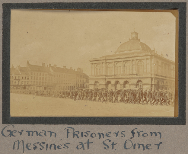 Gruppe deutscher Kriegsgefangener aus Messines vor einem Gebäude mit einem klaren blauen Himmel im Hintergrund, mit Text unten.