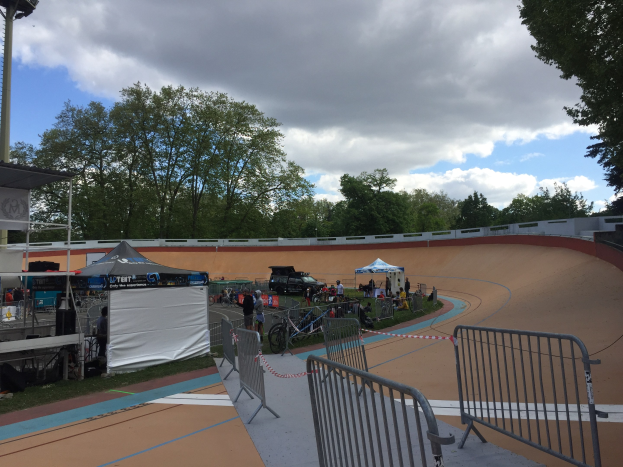 Gruppe von Radfahrern auf einer Schmutz-BMX-Strecke bei den UCI-BMX-Weltmeisterschaften 2018, mit Zelten, Fahrzeugen und Bäumen im Hintergrund.