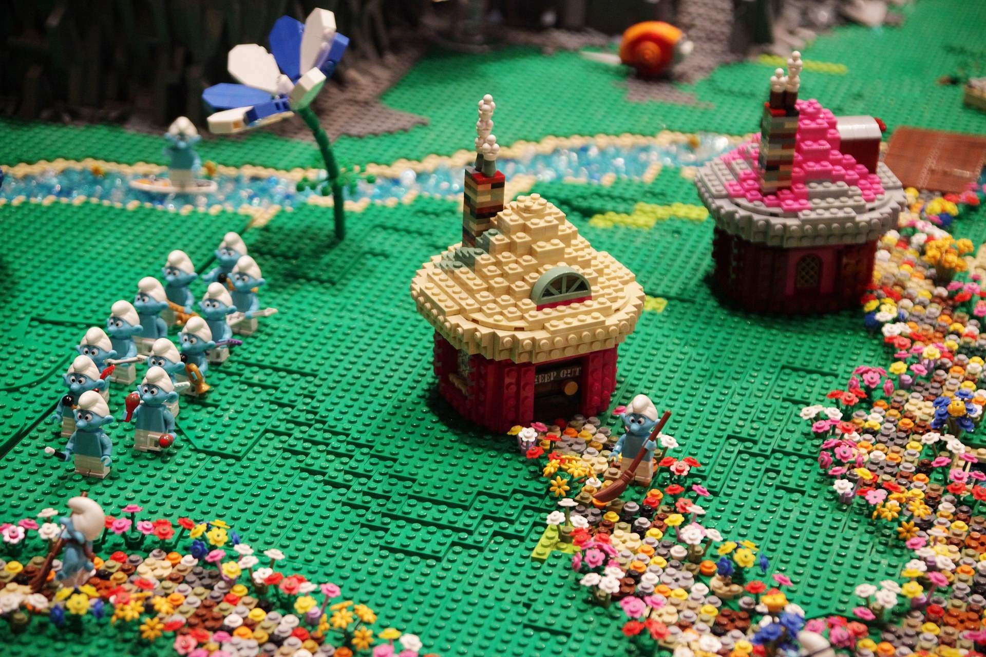 A Lego model of a small town with colorful flowers, toys, houses, plants, and other objects, set against a slightly blurred background.