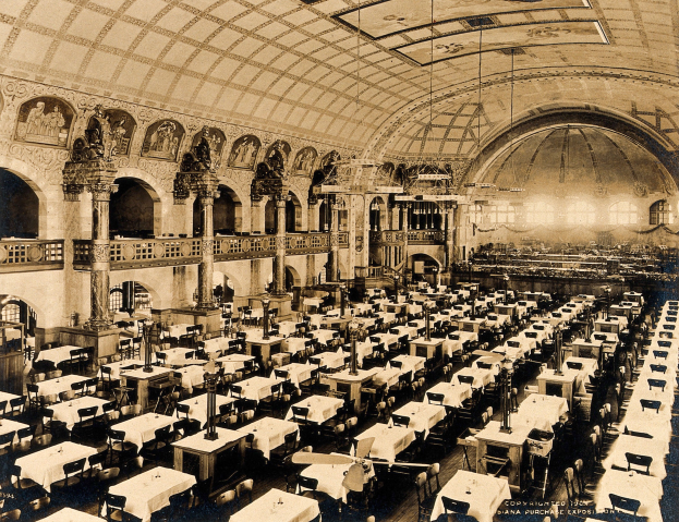 A vintage photograph of a large room with numerous tables and chairs, supported by pillars, featuring railings, wall sculptures, and ceiling lights.