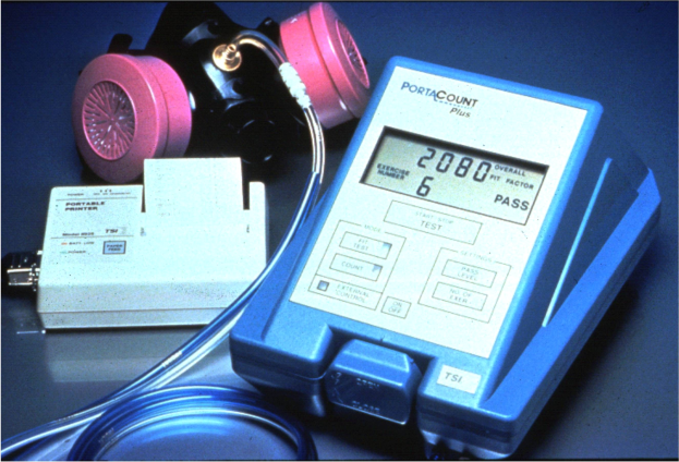 Gas mask on a table next to a gas detector device with a connected cable.