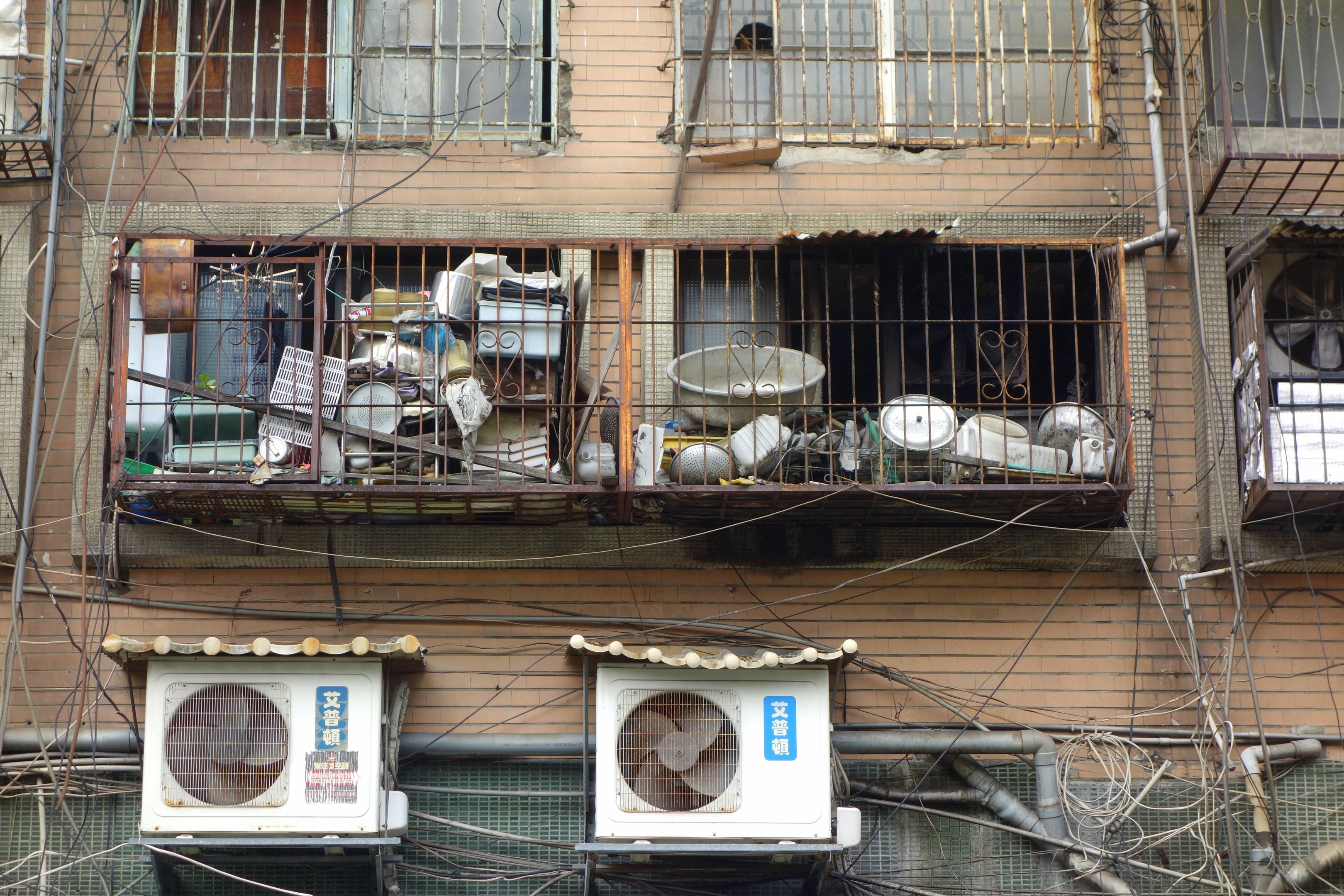 Wohngebäude mit Fenstern, Eisengittern, Klimaanlagen, Rohren und Kabeln an seiner Außenseite.