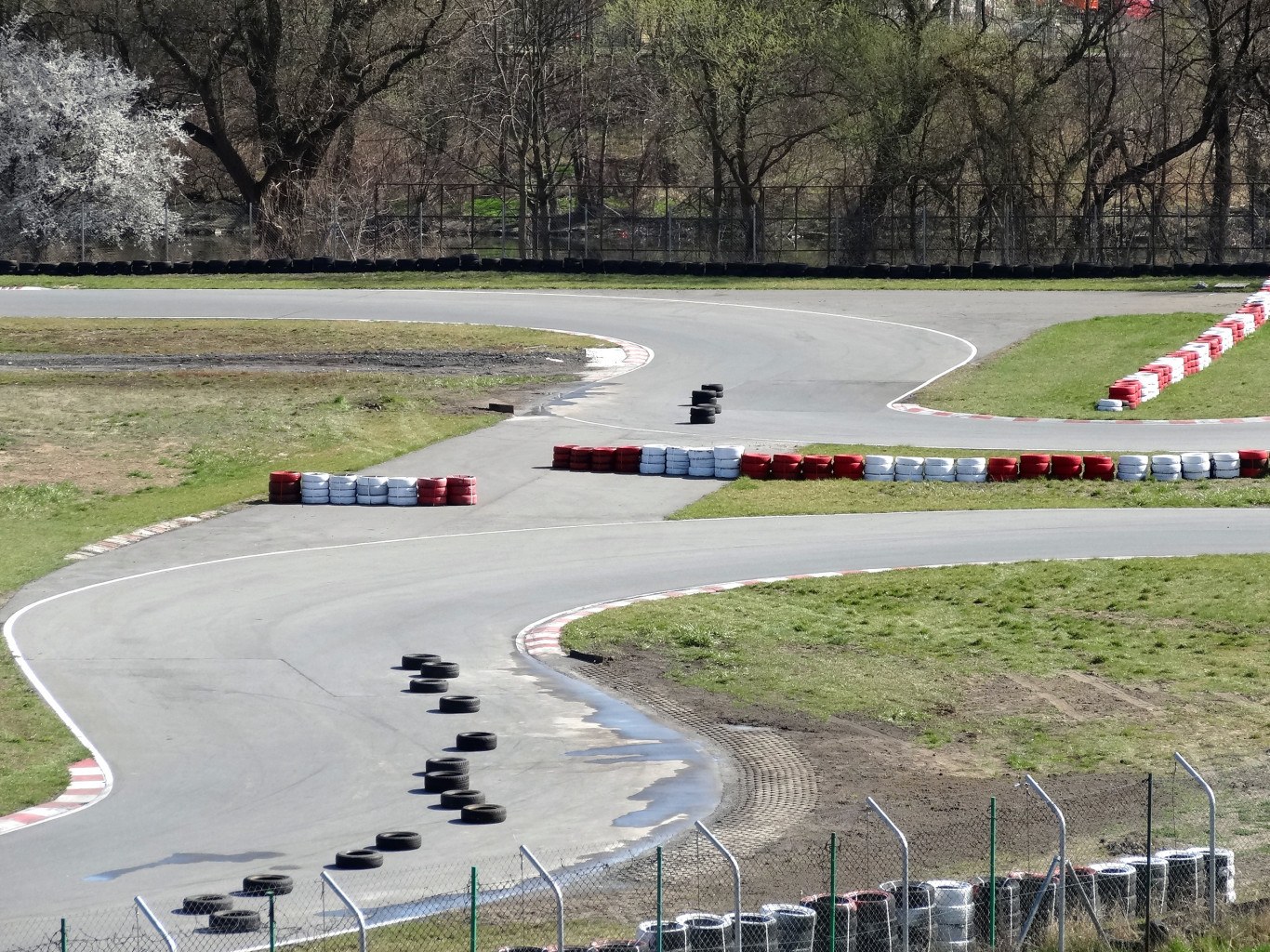 Rennstrecke voller Reifen, gesäumt von Gras und Maschendrahtzaun, mit Bäumen im Hintergrund
