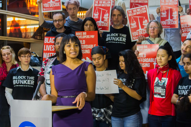 Eine Black-Lives-Matter-Aktivistin spricht an einem Pult mit Mikrofon vor einer Menge mit Schildern.