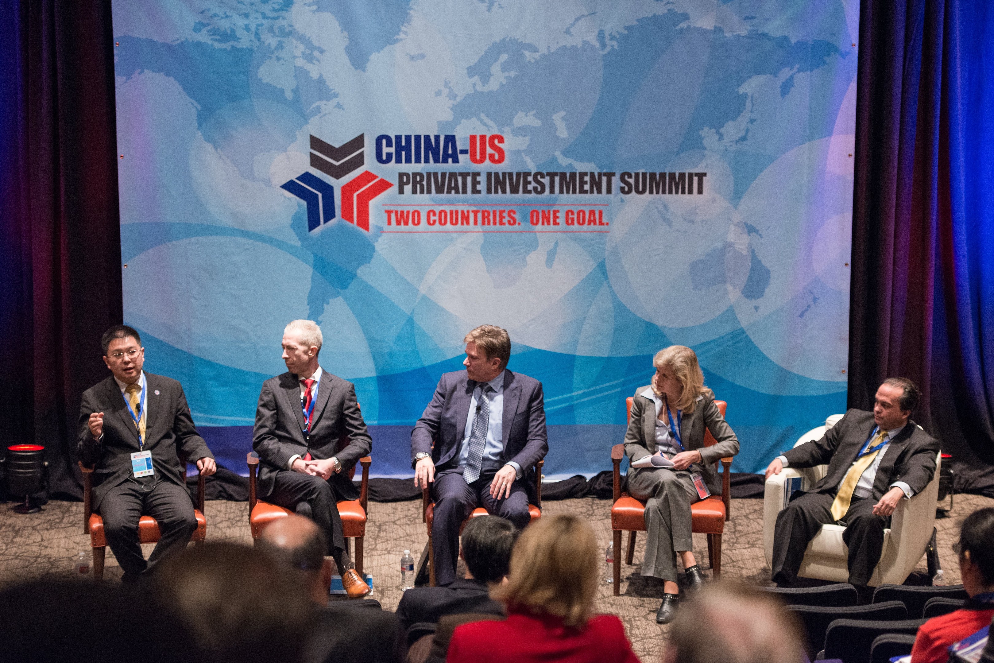 Eine Gruppe von Menschen, die auf Stühlen sitzen und auf einen Bildschirm schauen, auf dem Text und eine Karte angezeigt werden, mit Vorhängen im Hintergrund während eines China-US-Privatinvestment-Gipfels.