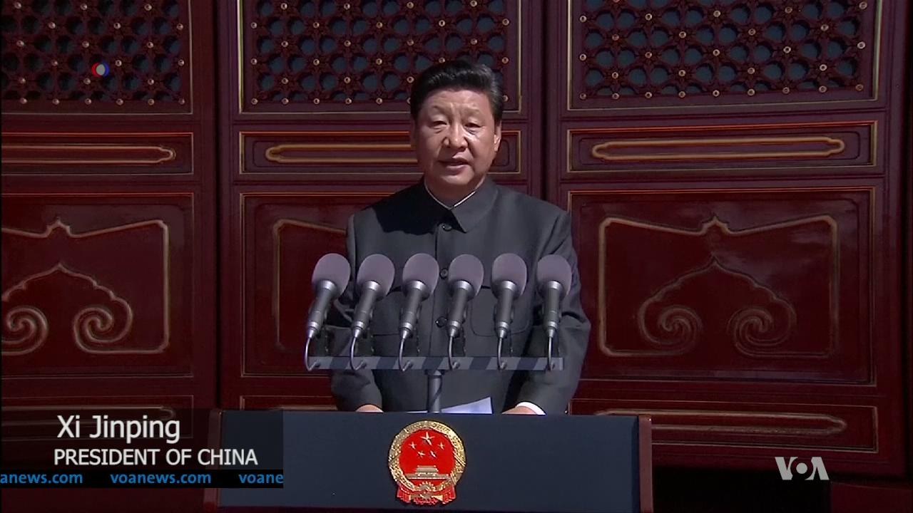Xi Jinping steht an einem Pult mit Mikrofonen und Logo, hält eine Rede in der Großen Halle des Volkes in Peking, mit einer hölzernen Wand im Hintergrund.