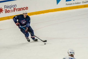Ein Hockey-Spieler auf dem Eis mit einem Stock in der Hand, der eine Sportuniform und einen Helm trägt, mit einerwand mit Text im Hintergrund.