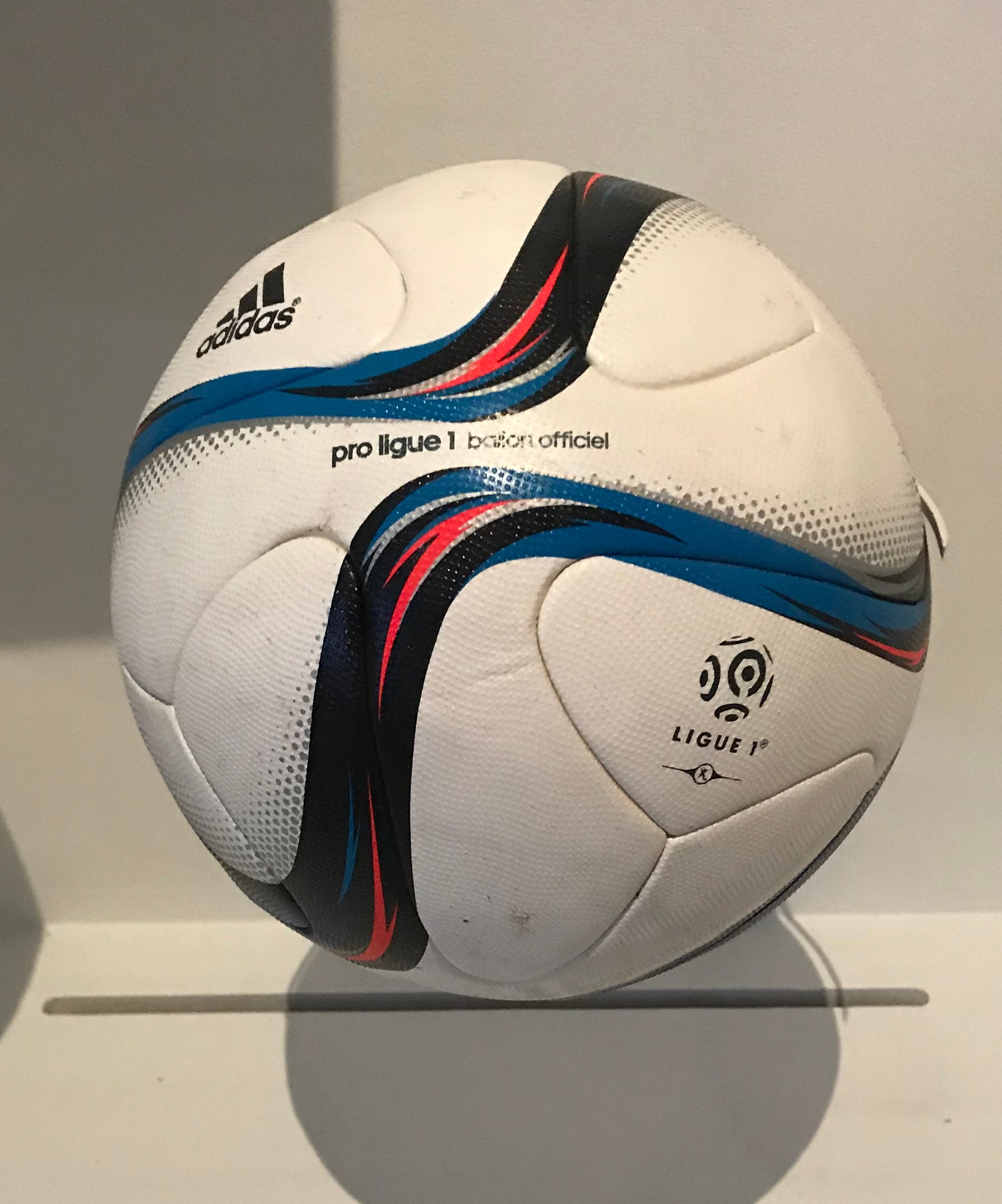 Ein weißer Fußball mit dem Adidas-Logo und der Aufschrift "Ligue 1" liegt auf einem weißen Tisch gegen einen hellen weißen Hintergrund.