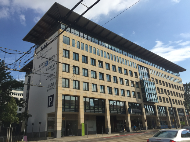 Large modern building with numerous windows, surrounded by trees and urban infrastructure, identified as the Stadthalle Center for Business in Cologne, Germany.