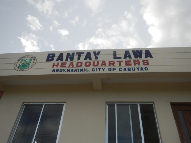 Ein zweistöckiges Gebäude mit Fenstern und einer Tür, beschriftet mit "Bantay Lawa Hauptquartier" in Cebu City, Philippinen, unter einem Himmel voller weißer Wolken.