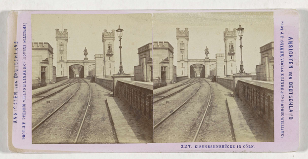 Schwarz-weiß-Stereoskopiebild einer Eisenbahnschiene mit der Eisenbahnbrücke in Köln, Deutschland, das Eisenbahnschienen, Wände, Stäbe, Statuen, Himmel und Text zeigt.