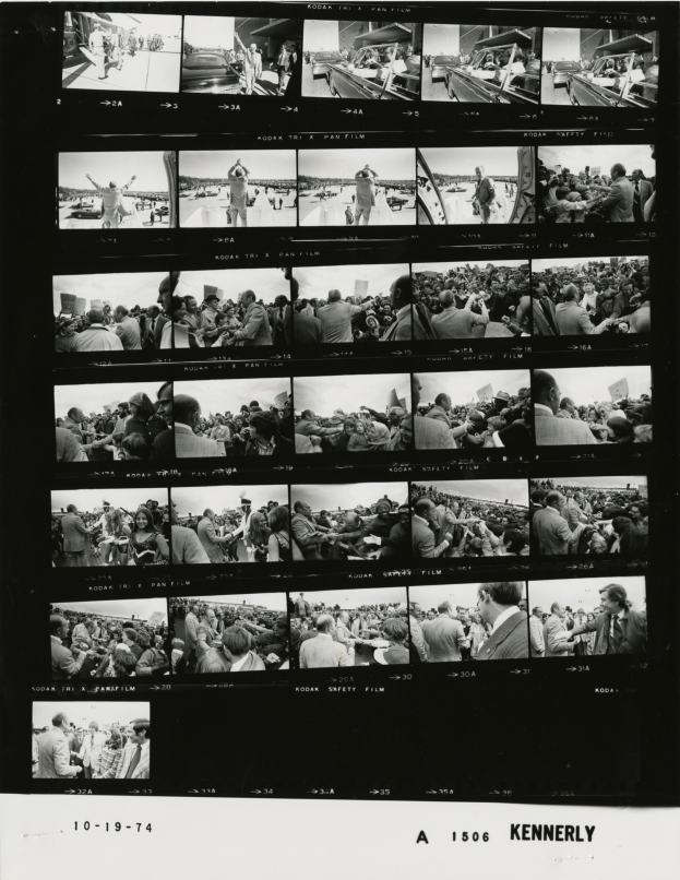 Ein Schwarz-Weiß-Foto einer vielseitigen Menschenmenge, die um einen Fernseher versammelt ist und in die Kamera lächelt.