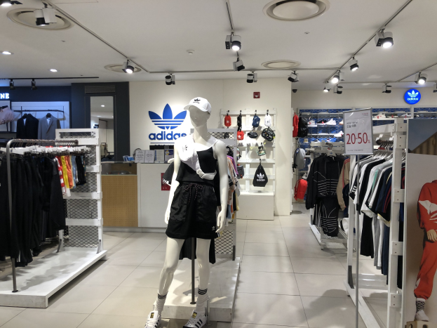Innenansicht eines adidas Einzelhandelsgeschäfts in Singapur mit Schaufensterpuppen, Kleiderständern, einer Texttafel und Deckenbeleuchtung.