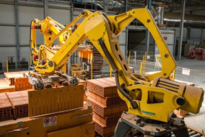 Großes Industriegelände mit gestapelten Kisten, Kränen, Zaun, Strommasten und einer fernen Wand in einer Fertigungsumgebung.