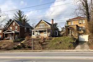Reihe von Häusern entlang einer Straße mit Fenstern, Türen, Säulen, Geländern, Stufen, Pflanzen, Gras, Bäumen und einem Pfahl mit einer Tafel unter einem bewölkten Himmel, repräsentiert eines der teuersten Häuser zum Verkauf in Detroit.