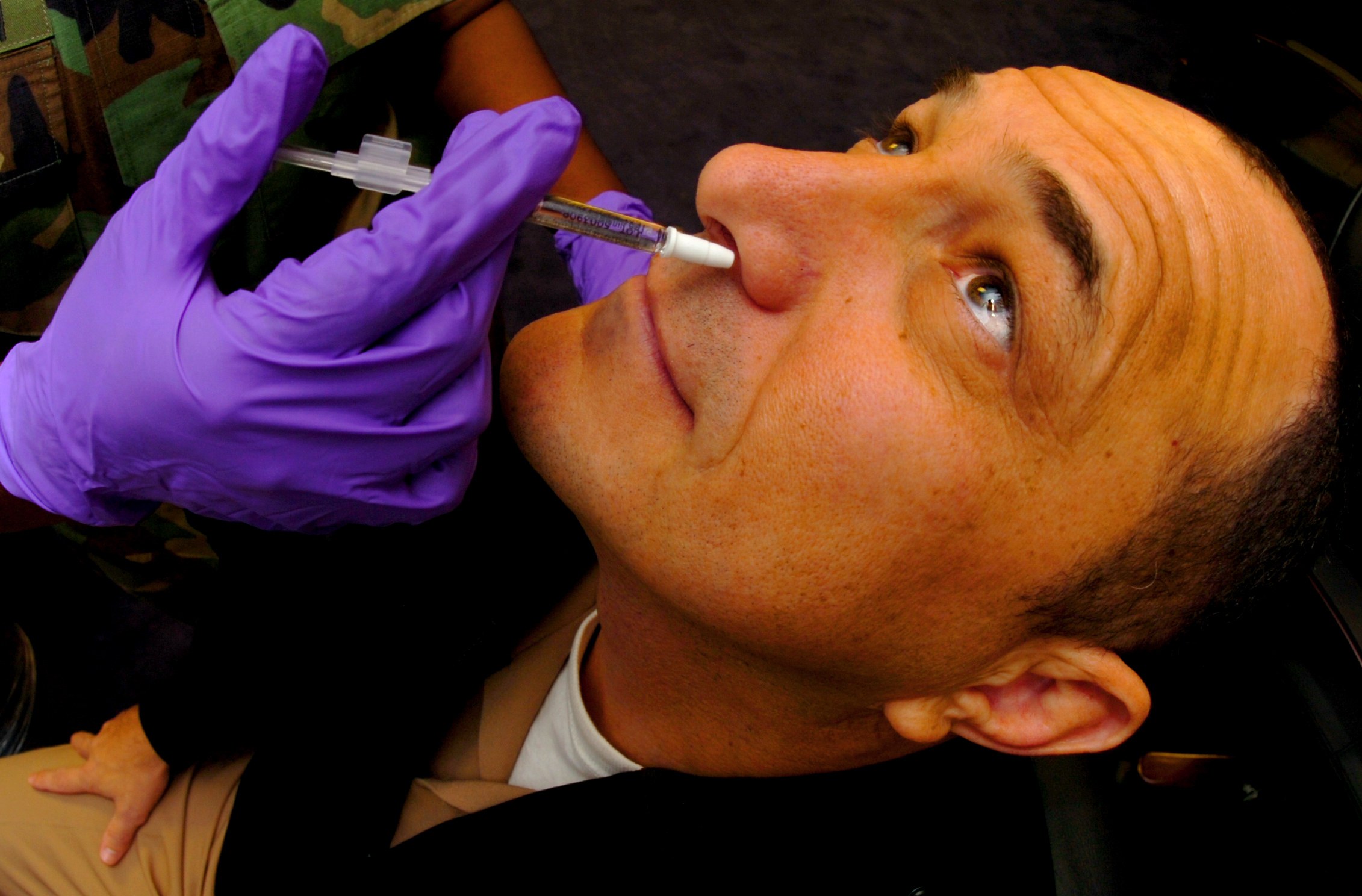 Ein Arzt in lila Handschuhen verabreicht einem Mann ein Vakzin mit einer Spritze im Mund.
